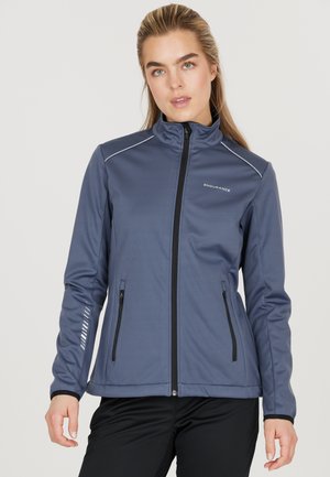Mörkblå atletisk jacka med dragkedja fram, hög krage, två fickor med dragkedja och reflexdetaljer på ärmarna. Tillverkad av ett glatt, stretchigt material.
