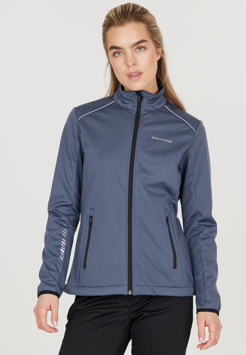 Veste de sport bleu marine avec fermeture éclair sur le devant, col haut, deux poches zippées et accents réfléchissants sur les manches. Fabriquée en tissu lisse et extensible.