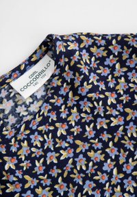 Niebieska tkanina w kwiatowy wzór z czerwonymi i żółtymi akcentami. Żebrowana struktura. Okrągły dekolt, z metką z logo "Coccodrillo".