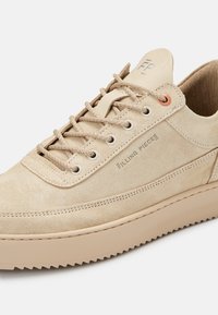 Beżowe zamszowe sneakersy z okrągłym noskiem, metalowymi oczkami i sznurowanym zapięciem; posiadają teksturowaną gumową podeszwę oraz tłoczone logo na języku.