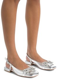 Zapatos planos metálicos plateados con punta cuadrada, diseño slingback y un acento decorativo de strass en la parte superior. Tacón bajo tipo bloque.