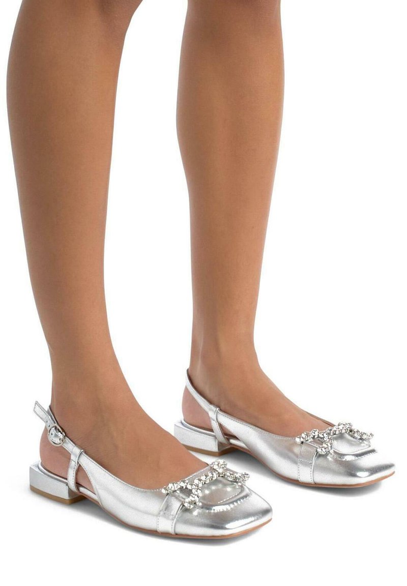Zapatos planos metálicos plateados con punta cuadrada, diseño slingback y un acento decorativo de strass en la parte superior. Tacón bajo tipo bloque.