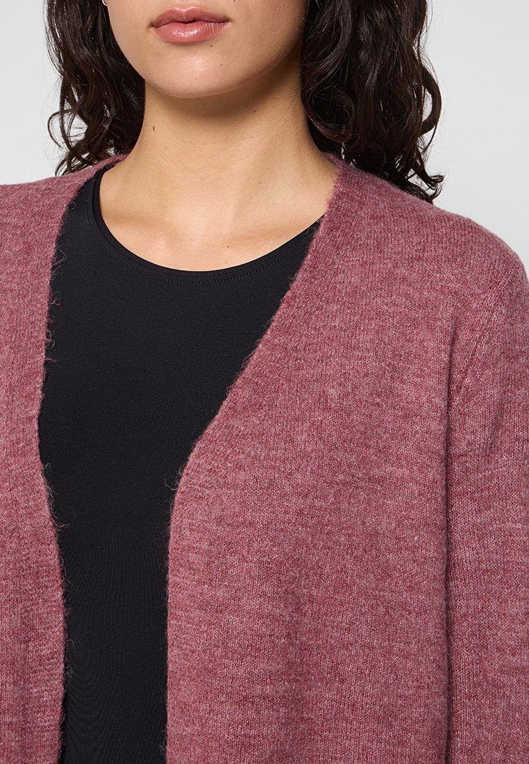 Cardigan de lana burdeos con un frente abierto y una textura ligeramente difusa, superpuesto a una blusa negra ajustada. Presenta un corte relajado y holgado.