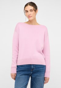 Helles Rosa, übergroßer Pullover mit weitem Bootsausschnitt, gerippten Bündchen und Saum. Hergestellt aus weichem Strickstoff, getragen über blauen Jeans.