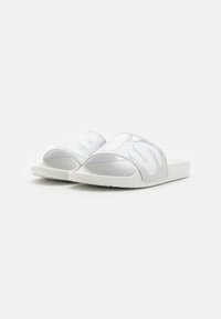 Sandales à talon blanc avec une bride translucide ornée d'un logo graphique audacieux, semelle plate et semelle extérieure texturée pour une meilleure adhérence.