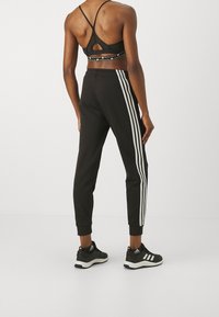 Joggers atléticos negros con rayas blancas a los lados, de corte ajustado y puños acanalados, combinados con un sujetador deportivo a juego.