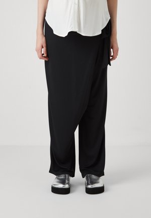 Black wrap pants made of smooth fabric, featuring a side tie detail. Paired with shiny silver platform shoes. Background is plain white.