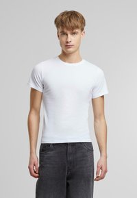 Hvit bomulls t-skjorte med korte ermer, rund hals og en tettsittende design. Brukt sammen med mørk grå jeans, noe som fremhever enkelhet og allsidighet.