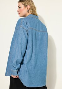 Camicia in denim azzurro chiaro con vestibilità rilassata, caratterizzata da dettagli in perle sulle maniche, colletto e polsini standard.