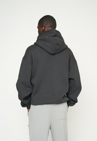 Sudadera de gran tamaño en gris oscuro con una capucha grande, mangas acanaladas y un corte relajado, combinada con pantalones en gris claro. Textura mate.