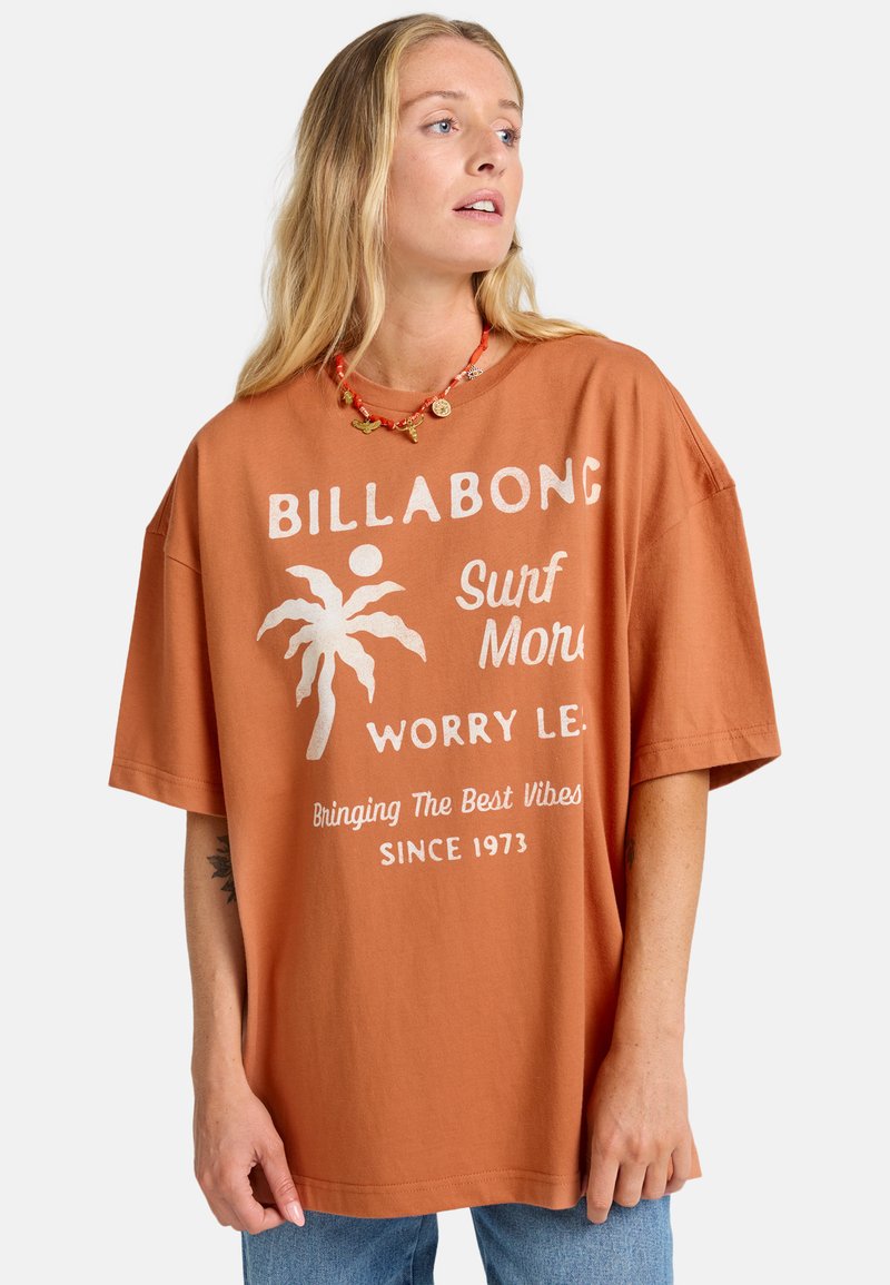 Camiseta de gran tamaño de color óxido, hecha de algodón, que presenta un gráfico de palmera blanca y un diseño de texto. Mangas cortas y corte relajado.