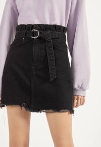 Černá džínová mini sukně s odstávajícím lemem, vysokým pasem a volánkovým pasem. Obsahuje tkaninový pásek se stříbrnou sponou.