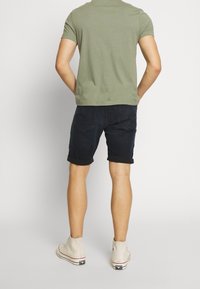 Mörka denimshorts med rullade nederkanter, kombinerade med en figurnära t-shirt i olivgrön bomull och beiga högskurna sneakers.