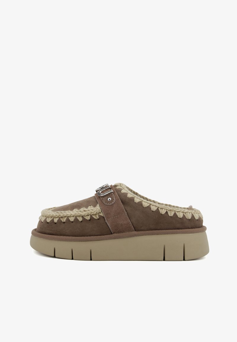 Scarpa slip-on in suede marrone con un accento intrecciato beige e dettaglio in fibbia argentata, dotata di una suola beige spessa e texture.