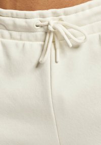 Hvite bomulls joggebukser har en snor i livet med hvite plastspisser og et mykt, teksturert stoff, designet for komfort.