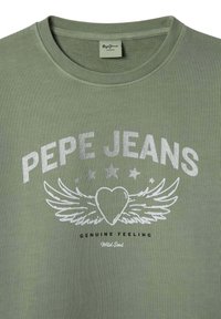 Camiseta de color verde oliva con textura acanalada, que presenta el texto gráfico plateado "PEPE JEANS", un diseño de alas y un corazón, y la frase "Genuine Feeling Wild Soul" debajo.