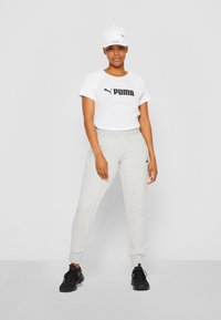 Hvid kortærmet t-shirt med sort "PUMA" logo, parret med lysegrå joggers og sorte træningssko. Hvid kasket med logo.