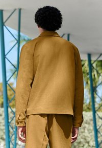 Camisa de color mostaza y pantalones a juego, ambos en un tejido texturizado. Presenta un cuello, puños abotonados y un corte relajado.