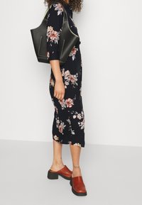 Černé květinové šaty s tříčtvrtečními rukávy, kombinované s černou kabelkou a hnědými sandály na klínovém podpatku.