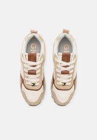 Baskets en cuir beige et suède, avec des accents marron, des lacets blancs et des éléments en or sur une semelle texturée.