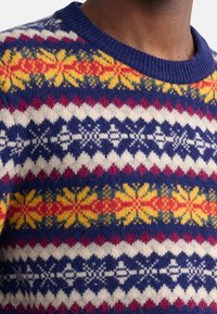Strickpullover mit einem bunten Muster aus Blumen und Rauten in Blau-, Gelb-, Rot- und Weißtönen, mit Rundhalsausschnitt und gerippten Bündchen.