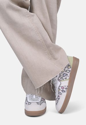 Hellbeige, weit geschnittene Hose trifft auf mehrfarbige Leo-Print-Sneaker mit grauen, rosa und grünen Akzenten sowie strukturierten Gummisohlen.