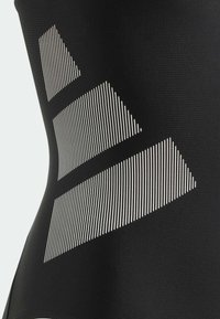 Sportieve zwarte bodysuit met witte lineaire patronen; beschikt over een gladde, rekbare textuur, een aansluitend ontwerp en geometrische vormen.