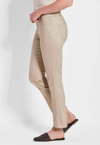 Pantaloni skinny beige con un motivo testurizzato, con vita media, due tasche posteriori e una finitura liscia. Abbinati a scarpe slip-on scure.
