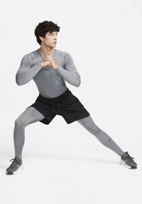 Treningsklær som inkluderer en tett grå langermet skjorte og svarte shorts, sammen med grå leggings og joggesko. Nike-logoen er synlig.