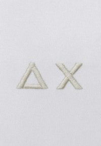Tessuto bianco con caratteri ricamati di un leggero beige che formano la lettera greca Delta (Δ) e la lettera X. Design semplice e pulito senza motivi.