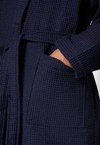 Navy blue waffle-textured bathrobe featuring a belted waist and a front pocket. The fabric shows a grid pattern for added texture.