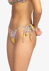Bikini bottom in pastel floral pattern with yellow, pink, and green accents. Ties at the sides, showcasing a textured design.