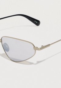 Óculos de sol de metal prateado com uma forma geométrica, lentes cinzentas e hastes pretas. Detalhes angulados notáveis nas hastes.