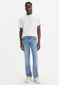 Camiseta blanca de algodón combinada con jeans de mezclilla azul claro. El modelo lleva zapatos de color crema. Diseño sencillo, corte relajado, sin patrones ni acentos visibles.