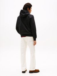 Felpa nera con cappuccio e cordino, jeans bianchi e scarpe marroni. Tessuto morbido, vestibilità rilassata, cuciture visibili sui jeans, design minimalista.