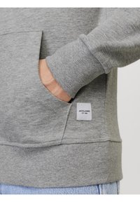 Grauer Pullover mit gerippten Bündchen und einer Kängurutasche. Verfügt über ein eingenähtes Etikett mit der Aufschrift "JACK & JONES" und "EST. 1990" nahe dem Saum.