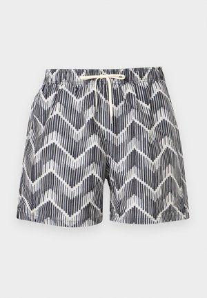 Herren-Badeshorts mit schwarz-weißem Zickzackmuster, elastischem Bund und weißer Kordel auf hellgrauem Hintergrund.