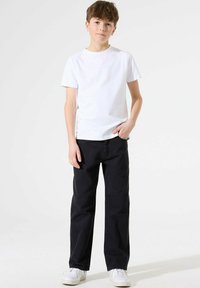 T-Shirt bianca in cotone con collo rotondo, abbinata a jeans dritti blu navy. Sneakers bianche completano l'outfit. Design semplice, senza motivi.