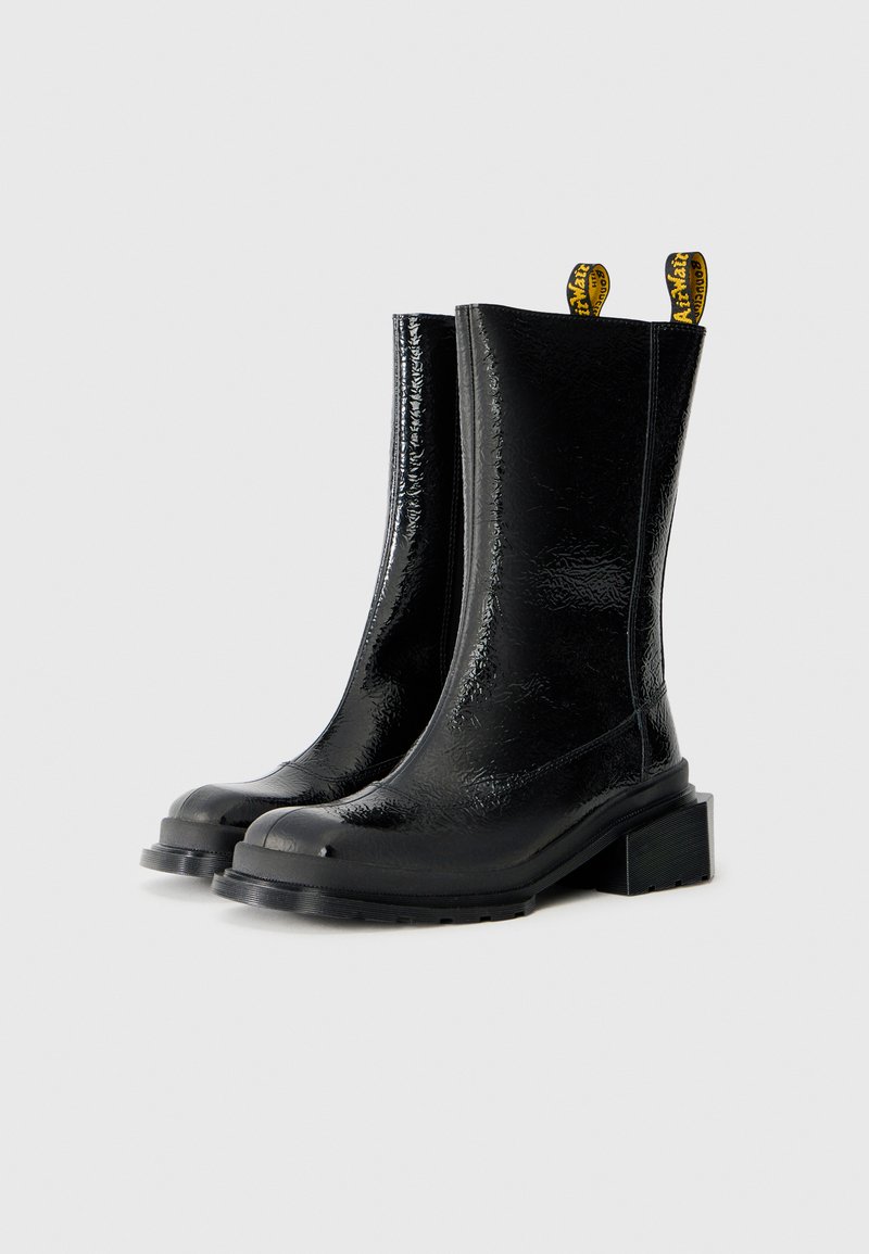 Zwarte glanzende enkelboots met een gestructureerde afwerking, een dikke blokhak en gele trekhulpjes. Minimalistisch ontwerp met ronde neuzen.