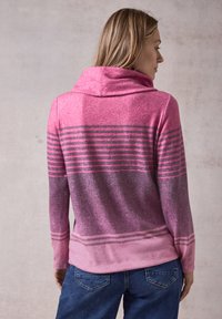 Kapuzensweatshirt in Rosa mit horizontalen grauen Streifen, aus weichem Material und mit lässigem Schnitt, kombiniert mit dunkelblauen Jeans.