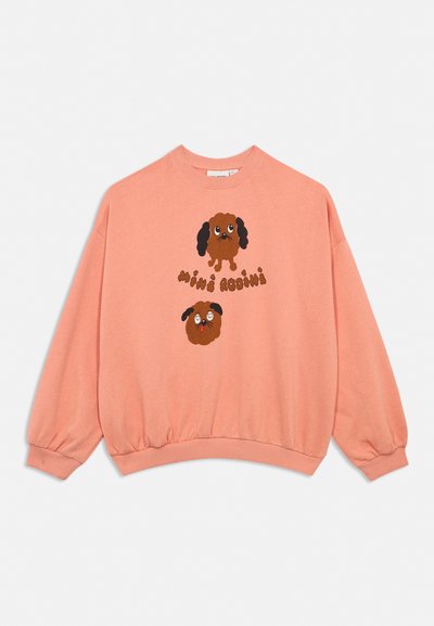 Sweatshirt à manches longues couleur pêche avec deux visages de chiens dessinés et le texte "mini rodini" en marron sur le devant, doté de poignets et d'un ourlet côtelés.