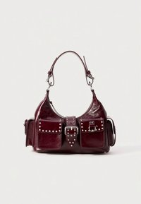 Vinröd läderhandväska med en böjd silhuett, nitar, två främre fickor och en silverdetalj med spänne på en bred rem.