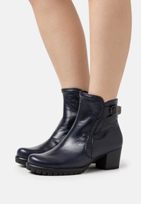 Botas de tobillo de cuero azul oscuro con un diseño elegante, que cuentan con una cremallera lateral, un tacón bajo y un hebilla decorativa.
