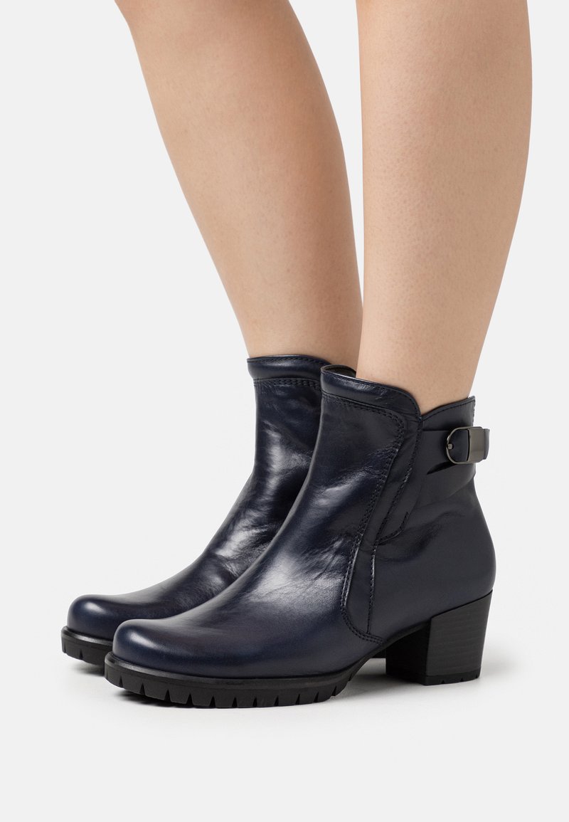 Botas de tobillo de cuero azul oscuro con un diseño elegante, que cuentan con una cremallera lateral, un tacón bajo y un hebilla decorativa.