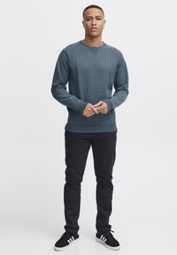 Sudadera azul oscuro con cuello redondo y puños acanalados, combinada con pantalones negros ajustados y zapatillas negras con franjas blancas.