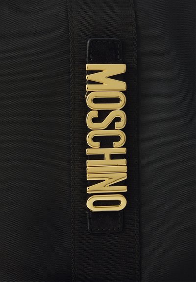 Juodas audinio maišas, puošiamas dideliu blizgiu auksiniu "MOSCHINO" logotipu; lygus paviršius su elegantišku dizainu ir kontrastine odos detalė.