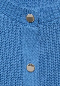 Cardigan tricoté bleu avec un motif texturé et trois boutons argentés proéminents au niveau de l'ouverture.