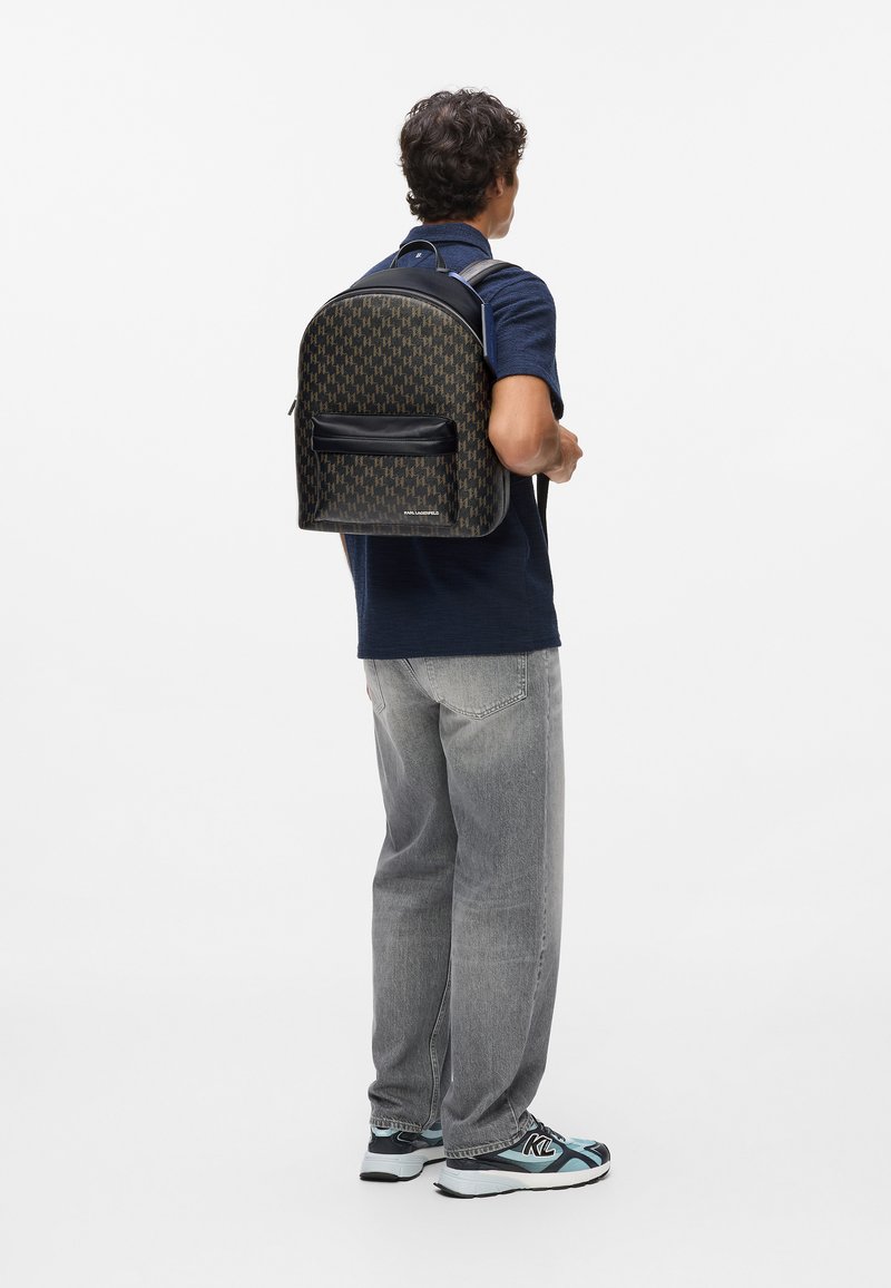 Fekete és barna mintás hátizsák, lekerekített formával, bőr kiegészítőkkel, elülső cipzáras zsebbel és állítható vállpántokkal.