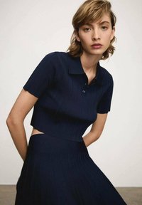 Námořnická pruhovaná crop top ve stylu s krátkými rukávy a límečkem, s knoflíkovým zapínáním a texturovanou tkaninou, spárovaná s odpovídající pruhovanou sukní.
