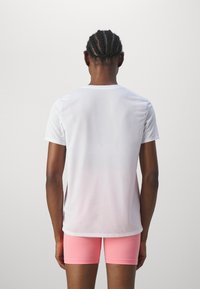 Camisa deportiva blanca de manga corta con una textura suave, que presenta un ligero degradado a rosa en la parte inferior. Combinada con pantalones cortos ajustados rosas.